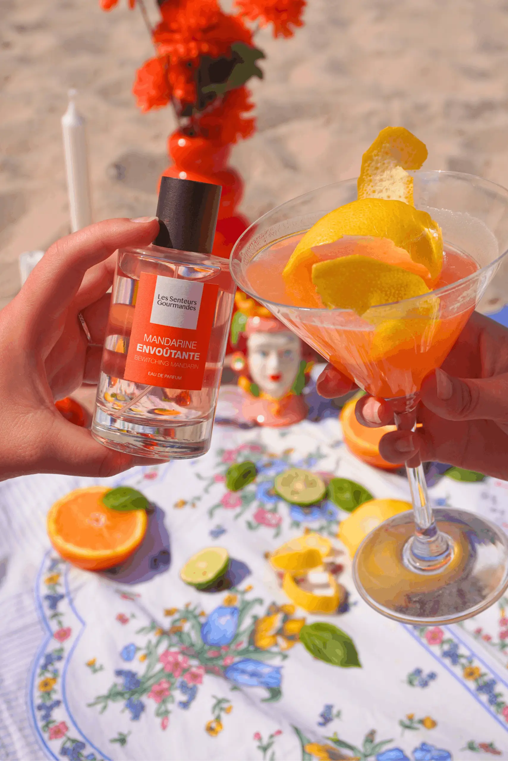 Flacon de parfum Mandarine Envoûtante Les Senteurs Gourmandes présenté avec un cocktail à l'orange et des agrumes frais